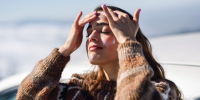 Žena ve svetru si nanáší na obličej krém.