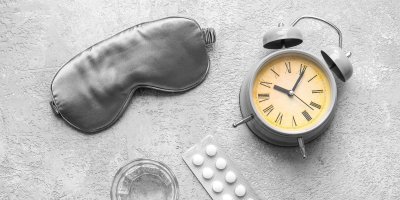 Maska na spaní, budík, sklenice vody a prášky