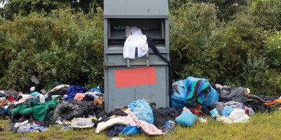 Plný kontejner na oblečení s kupami textilu na zemi