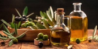 Dvě skleněné nádoby s olivovým olejem a čerstvé olivy na dřevěné desce