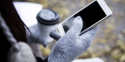 Žena v šedých pletených rukavicích drží smartphone