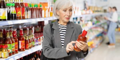 Starší žena si u regálu čte složení na láhvi s omáčkou