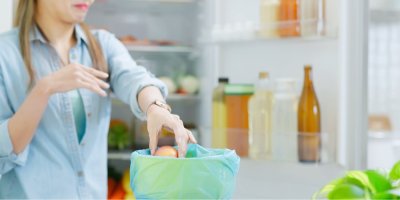 Žena uklízí lednici a vyhazuje prošlé potraviny do koše