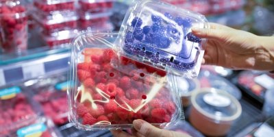 Žena drží plastové balení malin a ostružin.