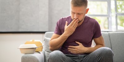 Muž sedící na sedačce cítí bolest břicha a nevolnost po konzumaci jídla