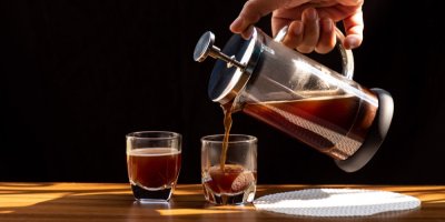 Člověk nalévá kávu z french pressu do dvou skleniček