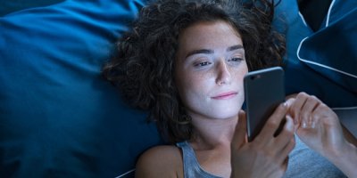 Mladá žena leží na posteli a dívá se do chytrého telefonu