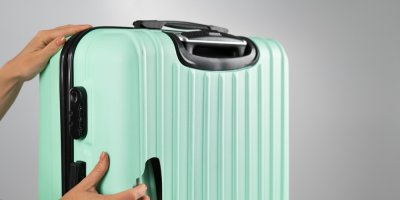 Ruce drží skořepinový kufr