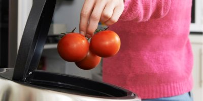 Žena hází rajčata do odpadkového koše.