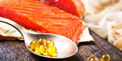 Záběr na kousky syrového lososa a před nimi lžíce s olejovými doplňky stravy