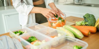 Žena drží misku zeleniny, kterou dává do krabiček