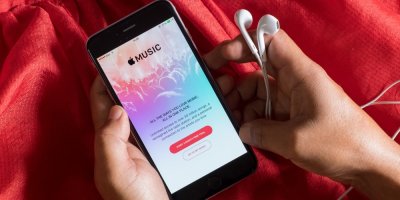 Člověk drží v rukou sluchátka a chytrý telefon s aplikací Apple Music na obrazovce 