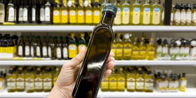 Muž drží v rukou dvě lahve s olejem v supermarketu