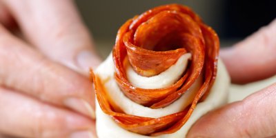 Ruce drží růžičku z pizza těsta se salámem