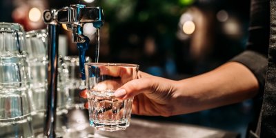 Barmanka nalévá vodu z kohoutku do sklenice