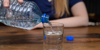 Žena sedící u stolu nalévá vodu z PET lahve do sklenice 