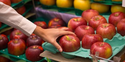 Ženská ruka si vybírá červená jablka v obchodě