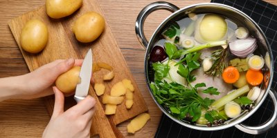 Ruce krájí slupku brambor vedle hrnce s vývarem
