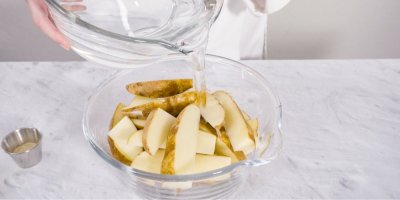 Člověk nalévá vodu do nádoby s nakrájenými bramborami