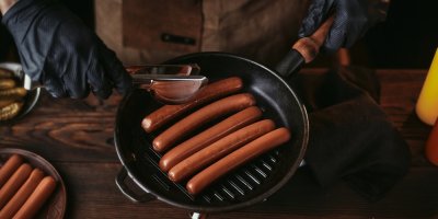 Kuchař připravuje párky na grilovací pánvi