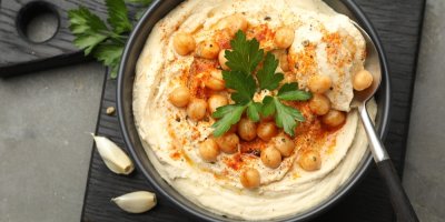 Hummus v misce ozdobený petrželkou, mletou paprikou a cizrnou na černém prkénku, pohled shora