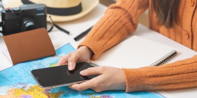 Žena plánuje dovolenou, drží telefon v ruce