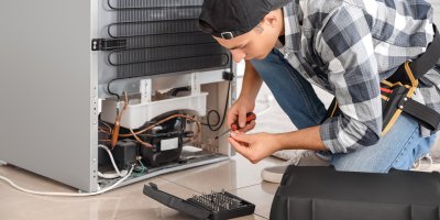 Opravář klečí u spotřebiče a drží šroubovák