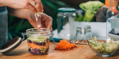Žena nakládá strouhanou zeleninu do fermentační sklenice