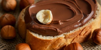 Veka namazaná Nutellou a okolo ní lískové oříšky