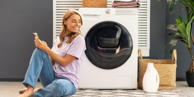 Žena sedí s mobilem u pračky