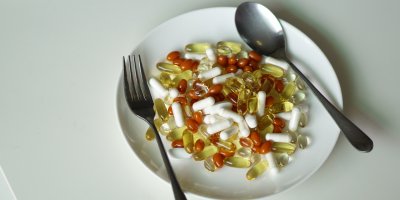 Talíř, na kterém jsou vysypané různé druhy vitamínových doplňků, vidlička, lžíce