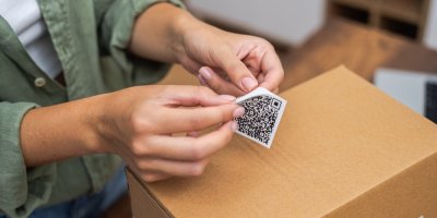Žena odlepuje nálepku s QR kódem a chystá se ji nalepit na krabici.