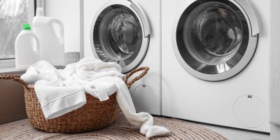 Pračka a sušička na prádlo, před ní bílé prádlo v koši