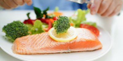 Talíř s plátkem lososa ozdobený citronem, v pozadí zelenina