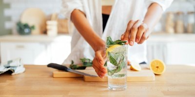 Voda s citronem a mátou na stole v kuchyni, v pozadí člověk