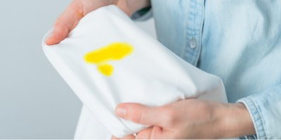 Ruce drží bílé tričko se žlutou skvrnou