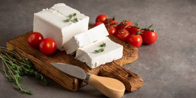 Pokrájená kostka balkánského sýra s rajčaty a bylinkami na dřevěném prkénku