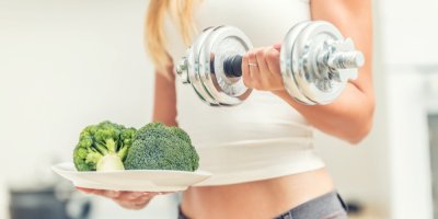 Žena drží v ruce činku a ve druhé ruce talíř s celou brokolicí