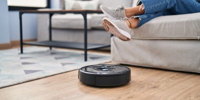 Robotický vysavač na podlaze a žena sedící na pohovce v obývacím pokoji