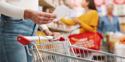 Mladá žena s nákupním vozíkem a nákupním seznamem v supermarketu