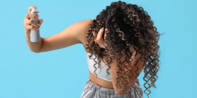 Mladá žena aplikuje vlasový sprej na své kudrnaté vlasy