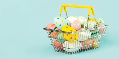 Barevná velikonoční vajíčka v nákupním košíku na modrém pozadí