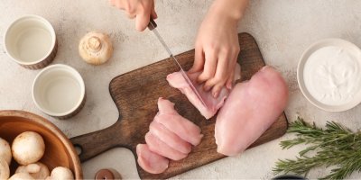 Žena krájí syrové kuřecí maso na dřevěném prkénku, pohled shora