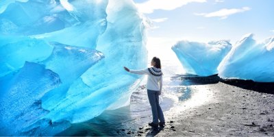 Žena stojí na pláži a dotýká se ledovce