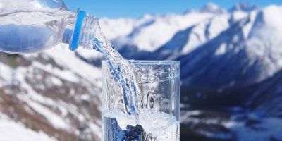 Nalévání vody z pet lahve do sklenice, v pozadí horská krajina