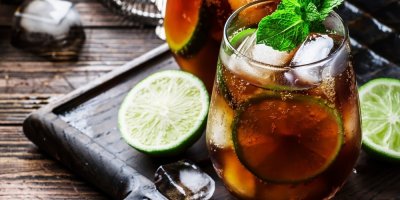 Koktejl načervenalé barvy, servírovaný s citronem, ledem a snítkou máty