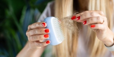 Žena odstraňuje z vlasového kartáče vypadané vlasy
