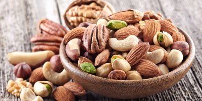 Kešu, mandle, pistácie, pekanové, lískové, para a vlašské ořechy v misce i kolem ní