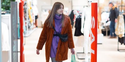 Mladá žena v obchodě prochází vstupem s bezpečnostním systémem proti krádeži 