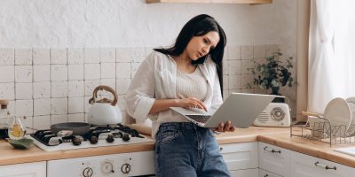 Mladá žena telefonuje, pracuje na počítači a vaří